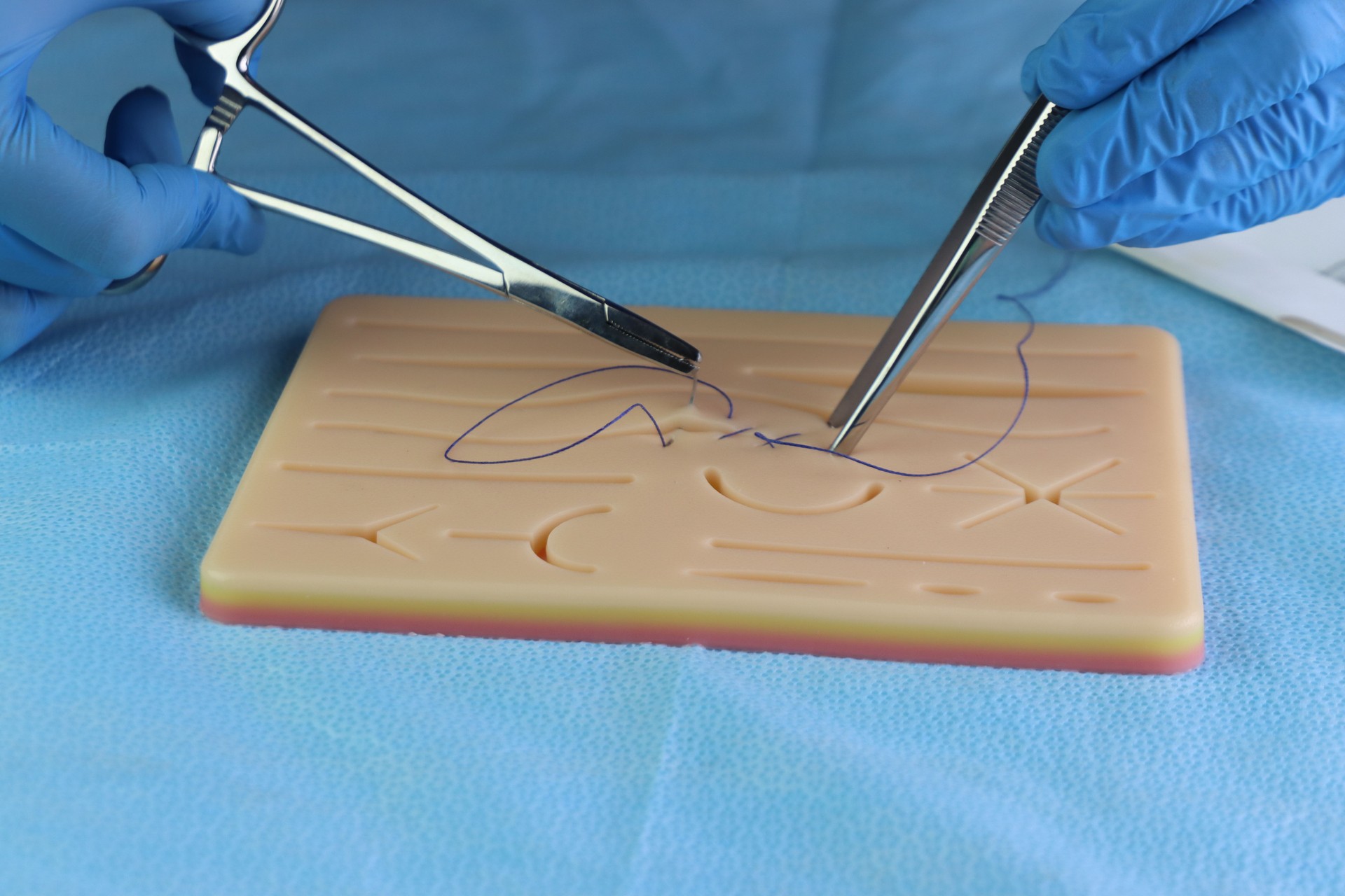 Healthcare professional wearing gloves training surgical suture with a needle in a wound simulation set. Close up in the surgical needle